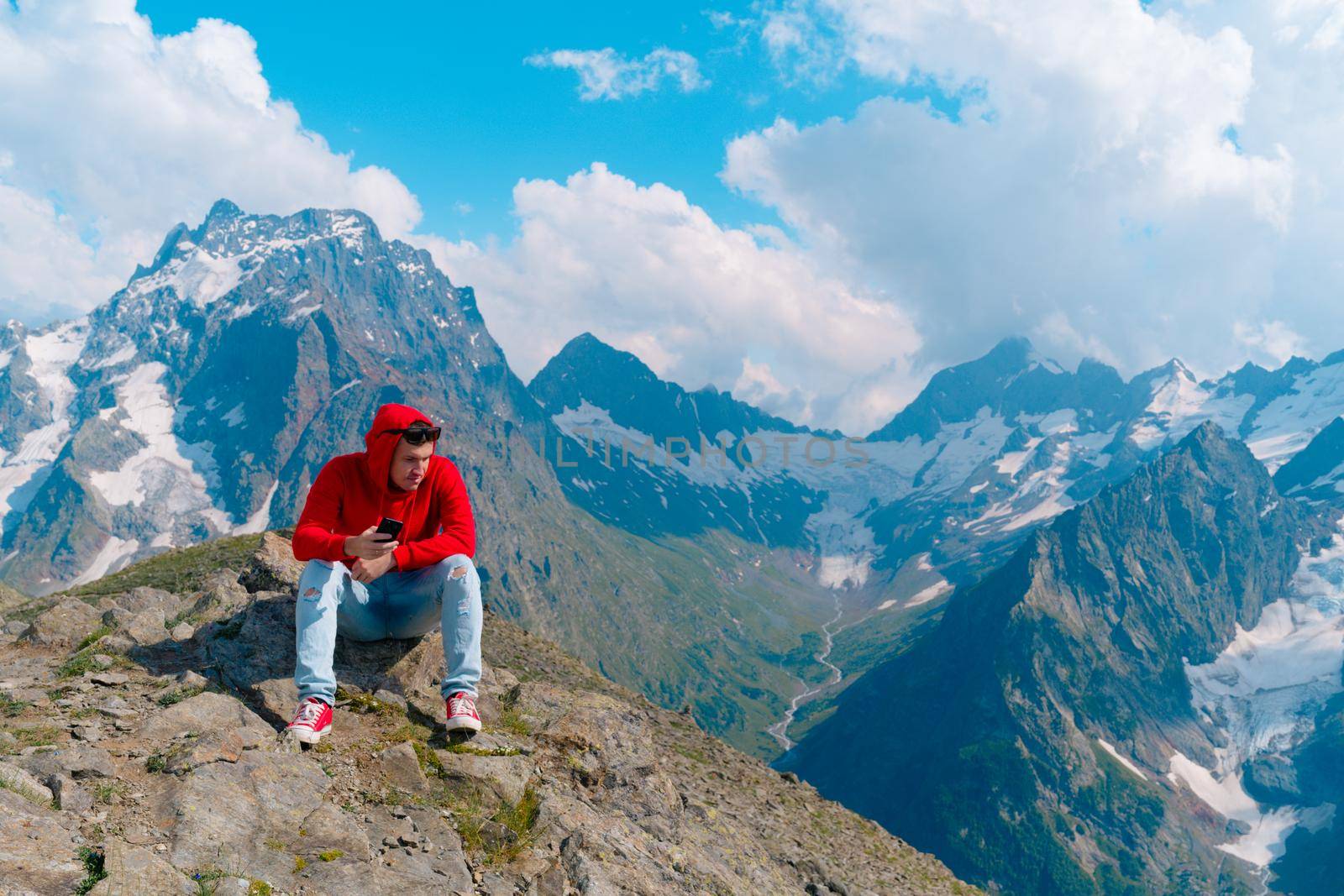 Adult male in red hoodie with hood enjoying beautiful view in mountainous area