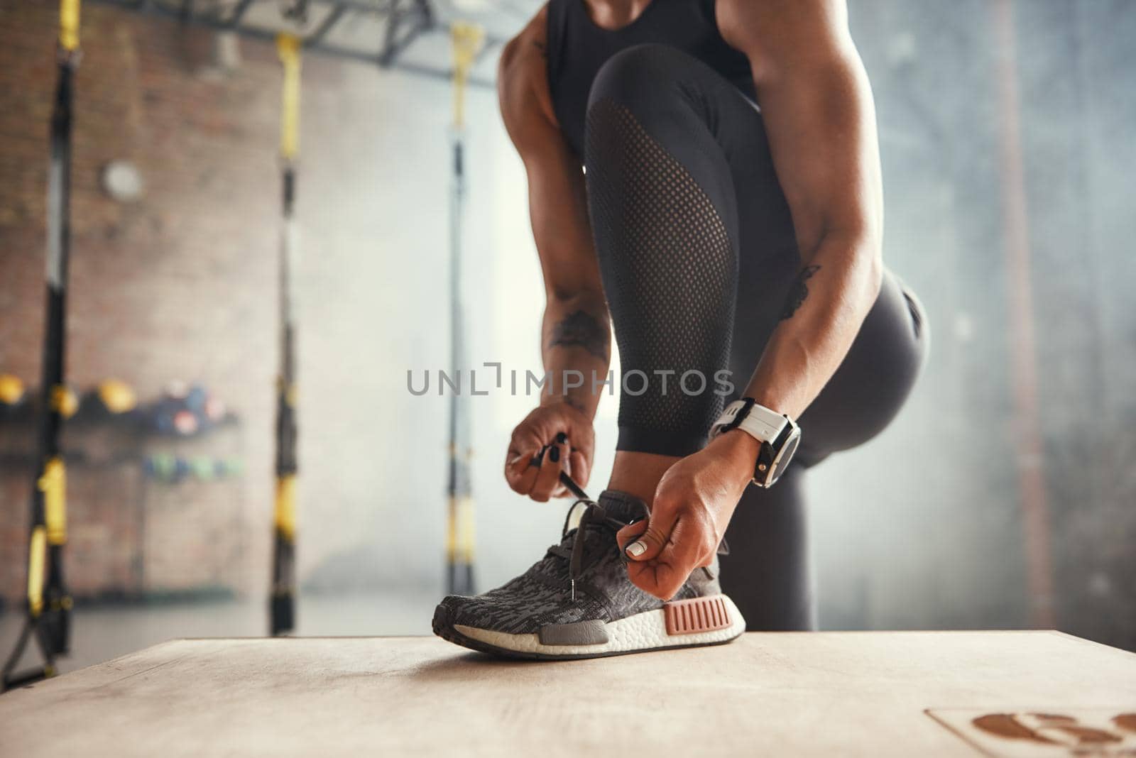 Preparing for workout. Cropped photo of beautiful young woman in sports clothing tying her shoelaces while exercising in gym. Professional sport. TRX Training. Healthy lifestyle