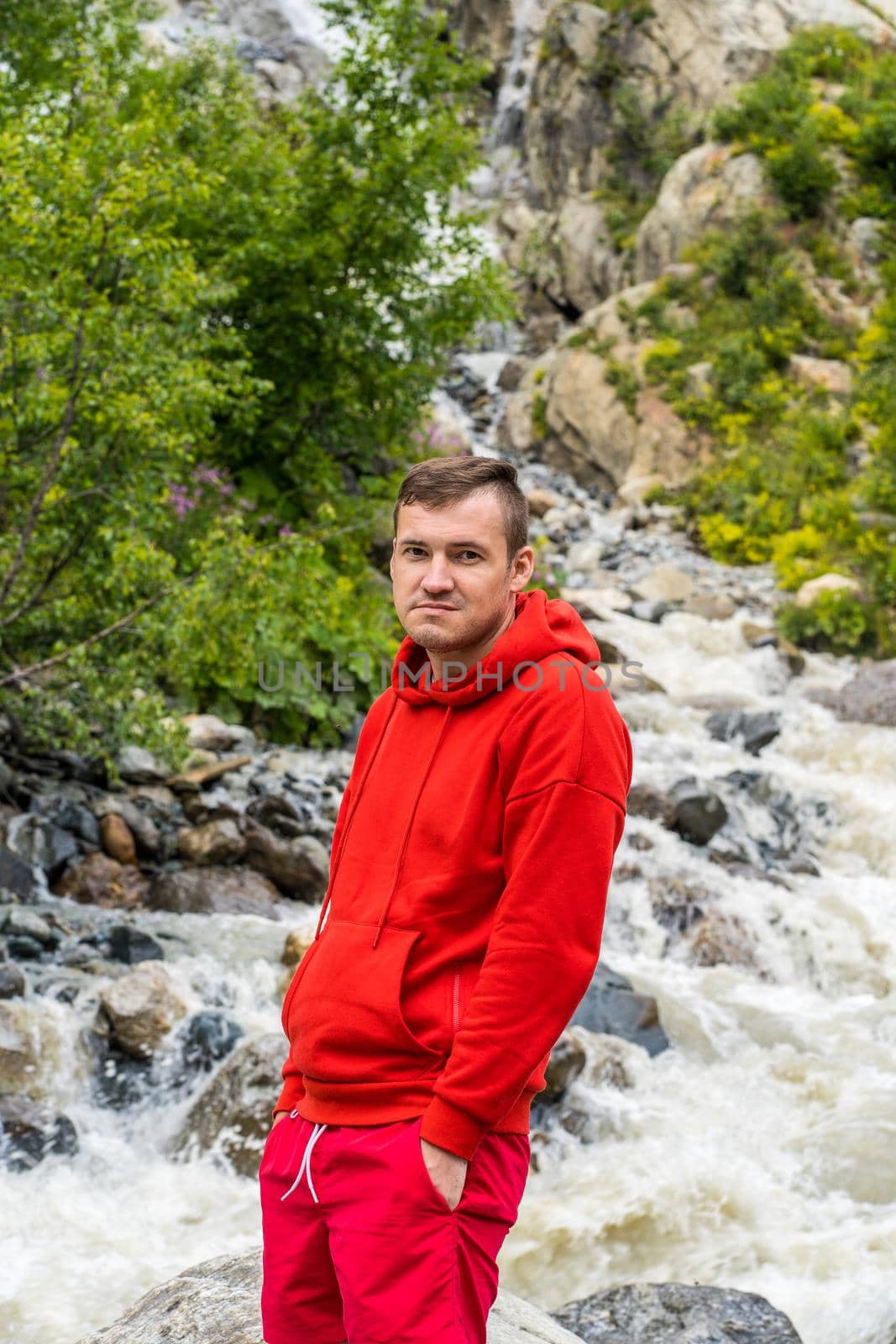 Portrait of young man looking away on background of waterfall. Adult male tourist enjoying beautiful view in mountainous area. by epidemiks