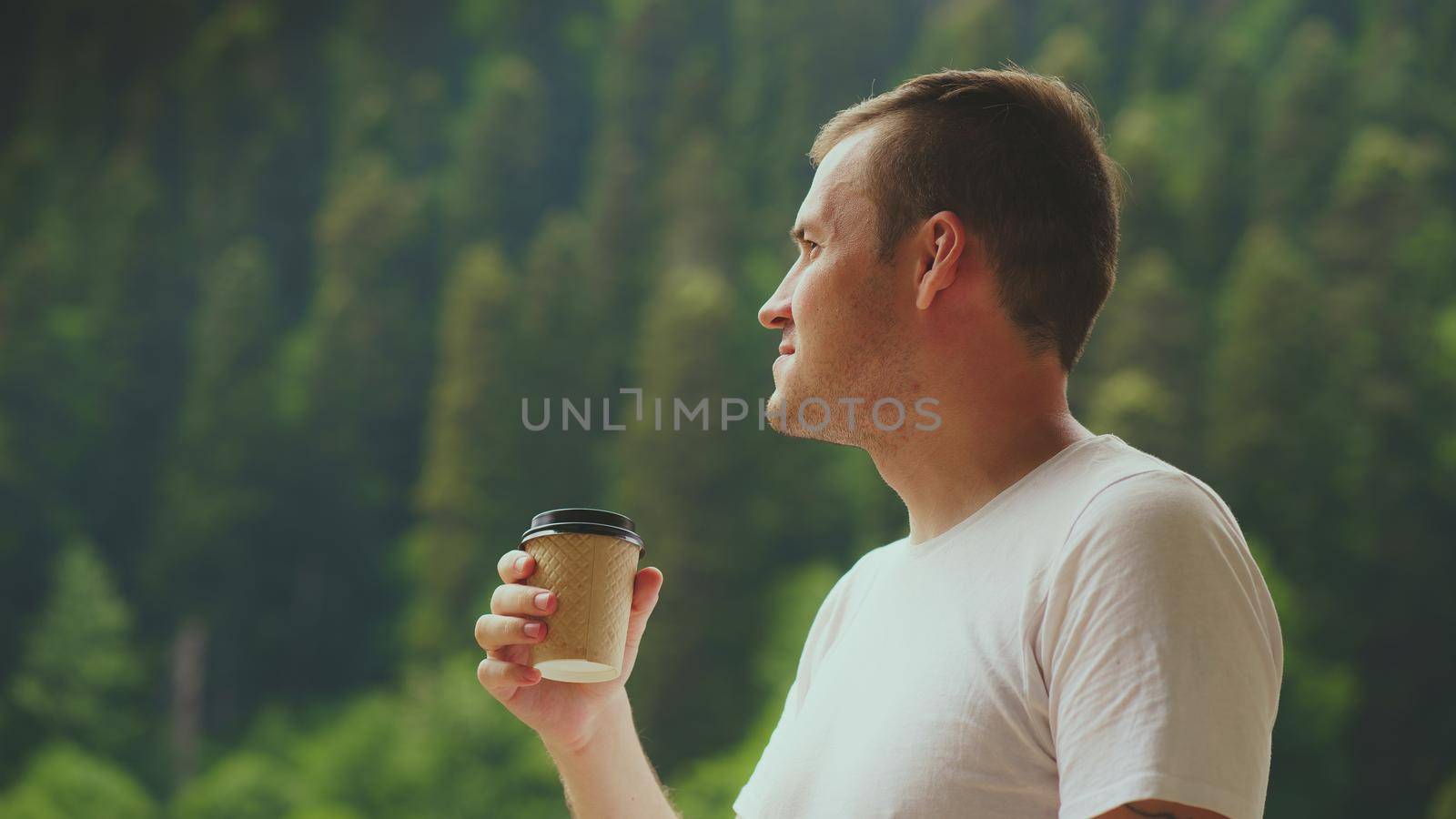 Portrait of pleasant guy spending time enjoying vacation and drinking coffee on background of mountain forest. Adult male enjoying hot drink against mountain landscape. by epidemiks