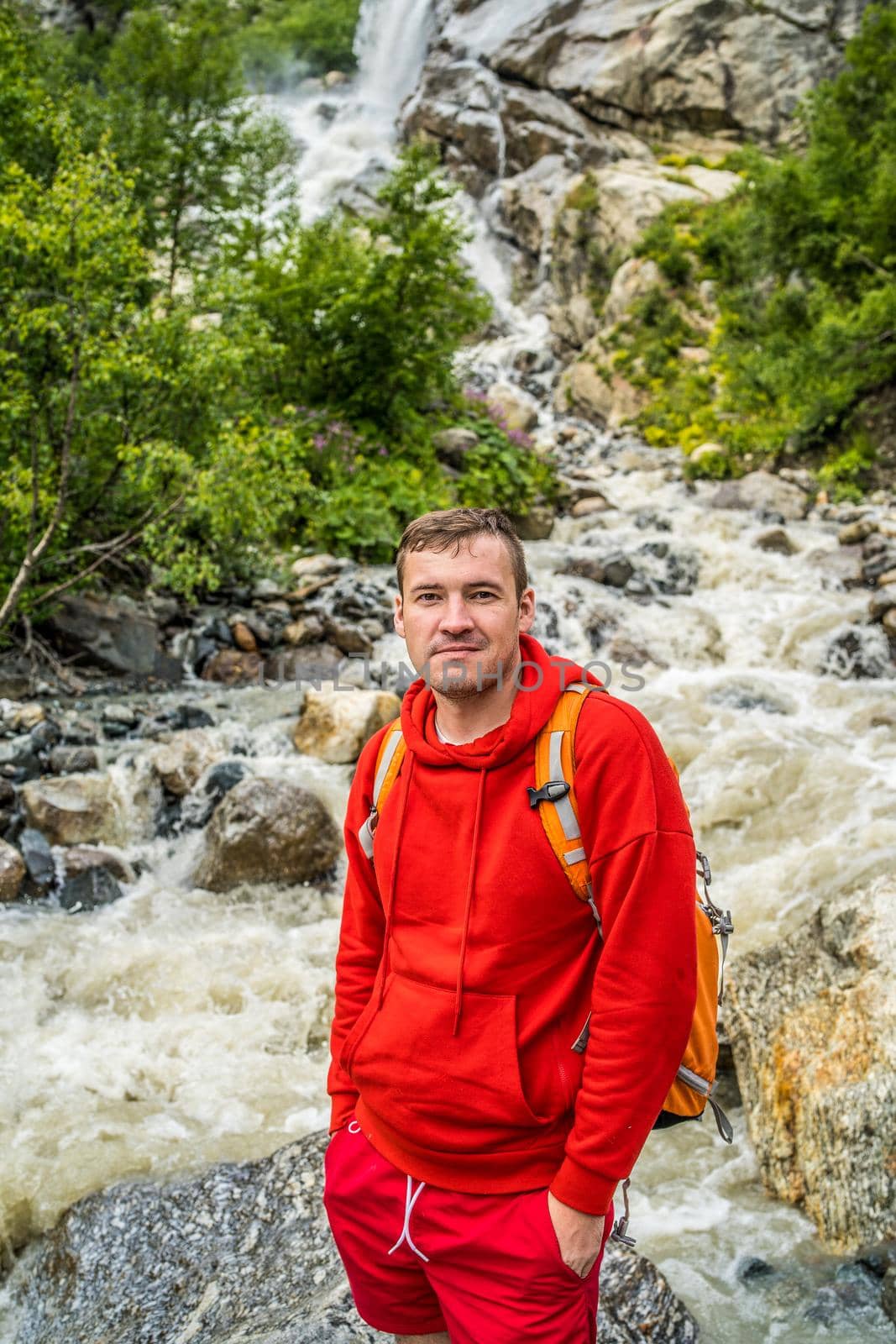 Portrait of young man looking away on background of waterfall. Adult male tourist enjoying beautiful view in mountainous area. by epidemiks