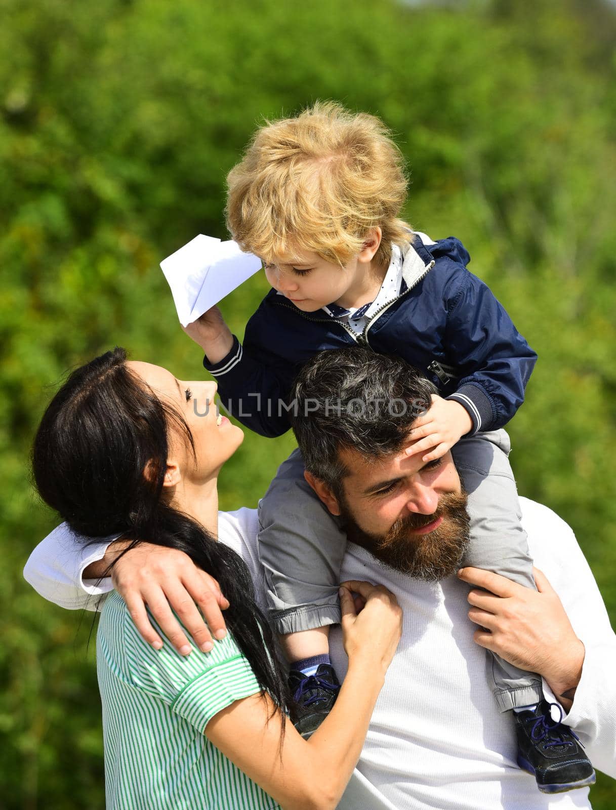 Happy family - mother, father and son on sky background in summer. Happy family - child son playing with paper airplane. Dream of flying. Cute boy with parents playing outdoor
