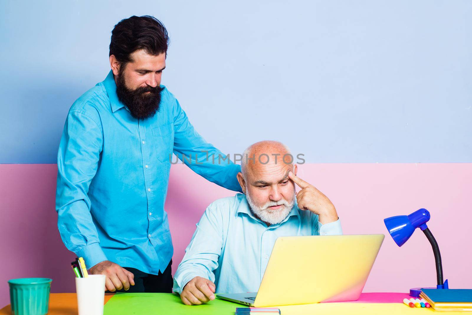 Two businessmen using computer together discussing news or movie. Old and young men looking at laptop screen watching movie or news in social network