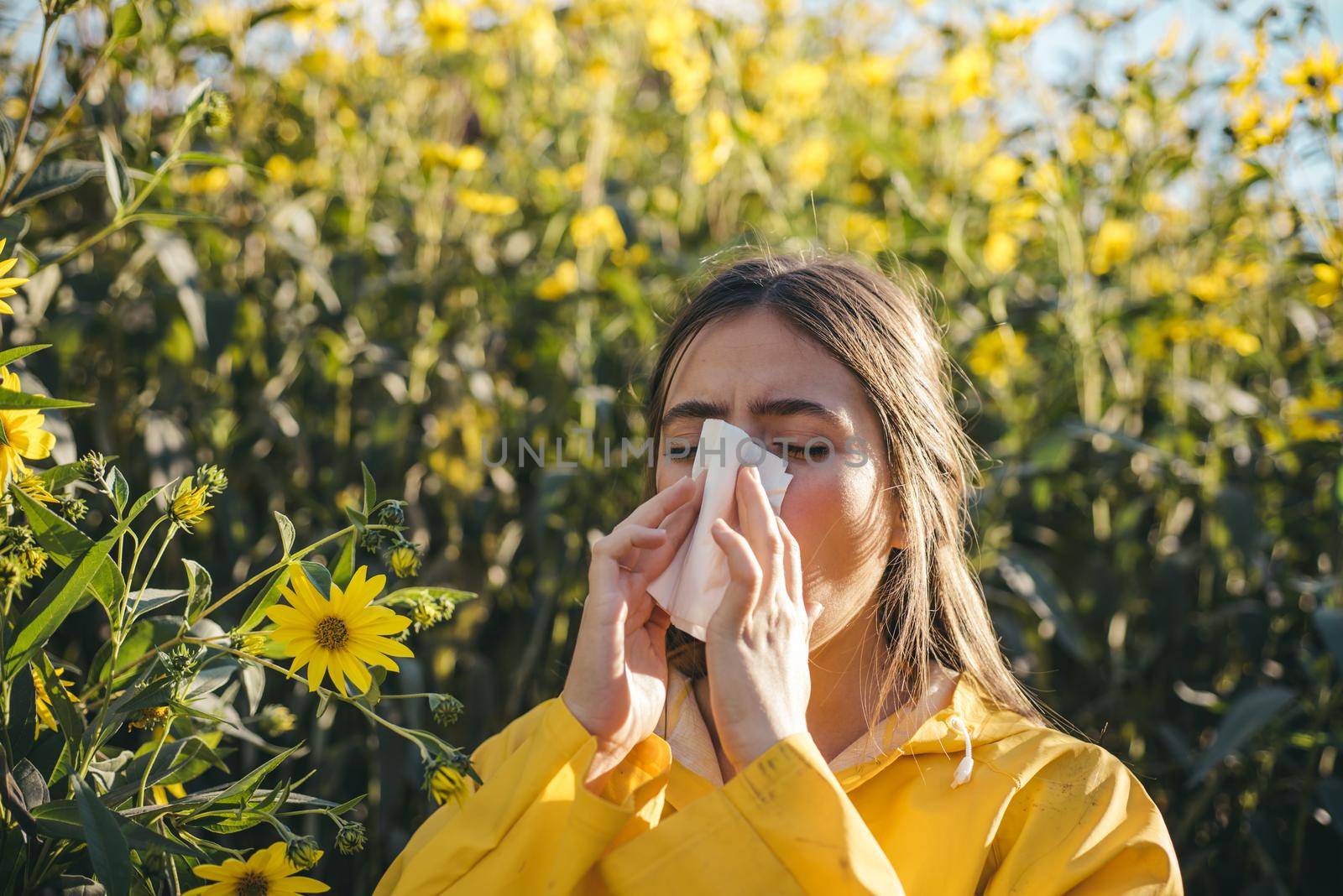 Woman with napkin fighting blossom allergie outdoor. Portrait of an allergic girl surrounded by seasonal flowers in bright yellow color. Beautiful girl having an allergic reaction to flowers