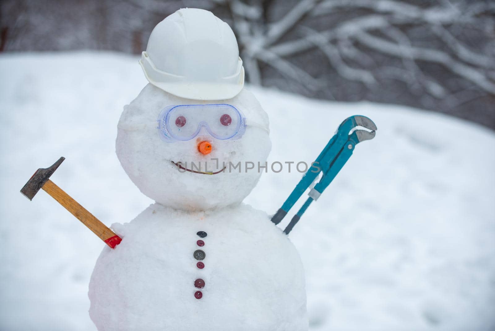 Snowman worker on snow background. Funny snowman in work helmet on snowy field. Handmade snowman in the snow outdoor