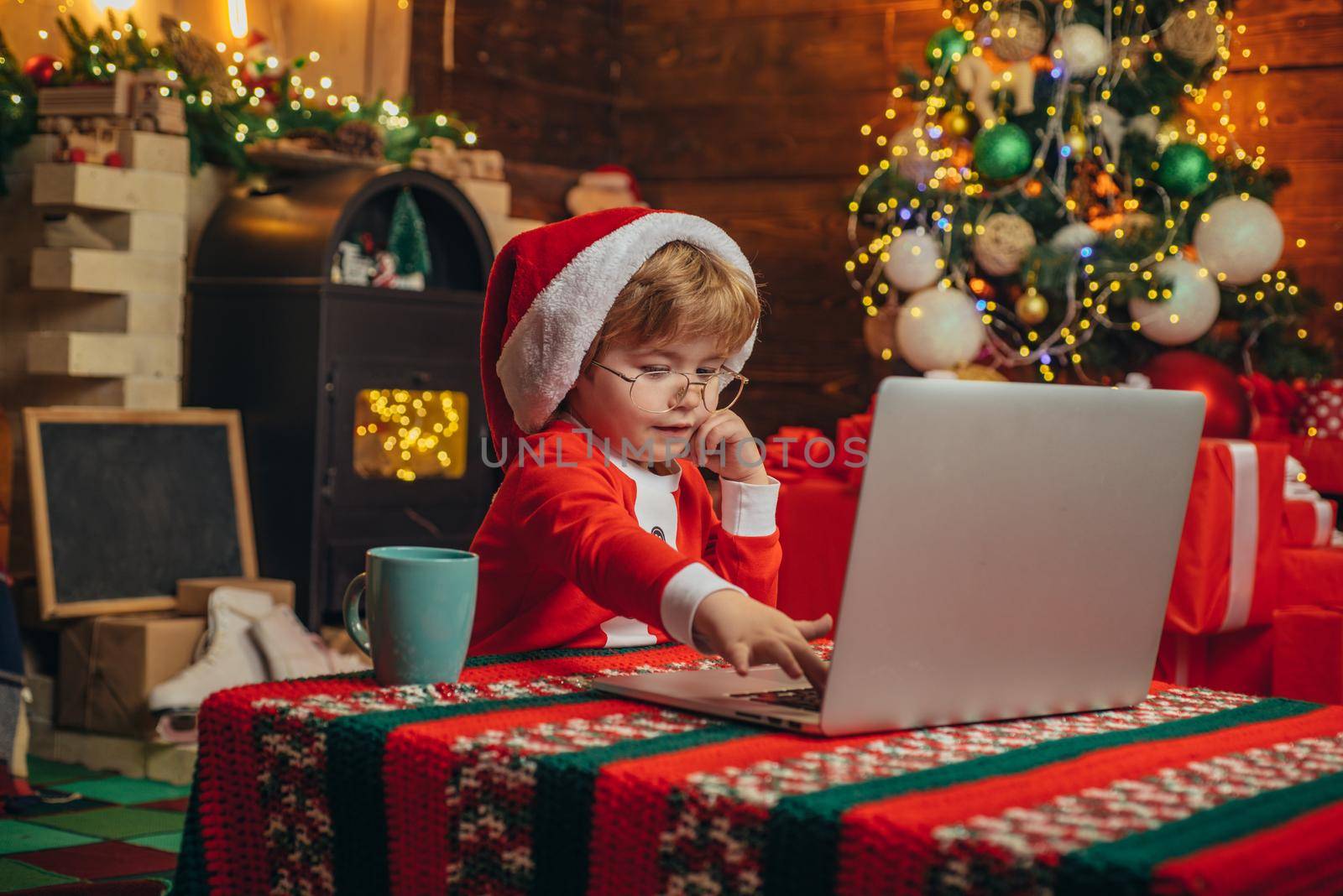 Gifts service. Smart toddler surfing internet. Helper of Santa with a Christmas magic gifts. Christmas. Home. Christmas time. Little boy in Santa hat and costume having fun