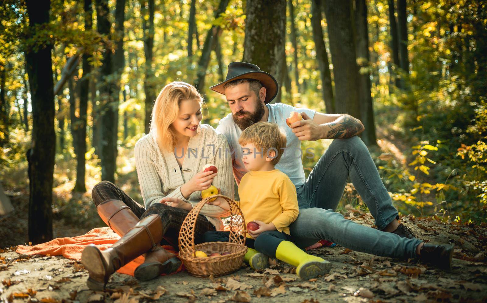A young family with small child having picnic in autumn nature at sunset. There is a basket with meal and toys for the kid. Young smiling family doing a picnic on an autumns day