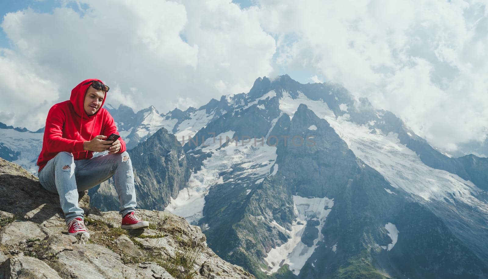 Male traveler using mobile phone against cloudy sky on sunny day in mountainous terrain.