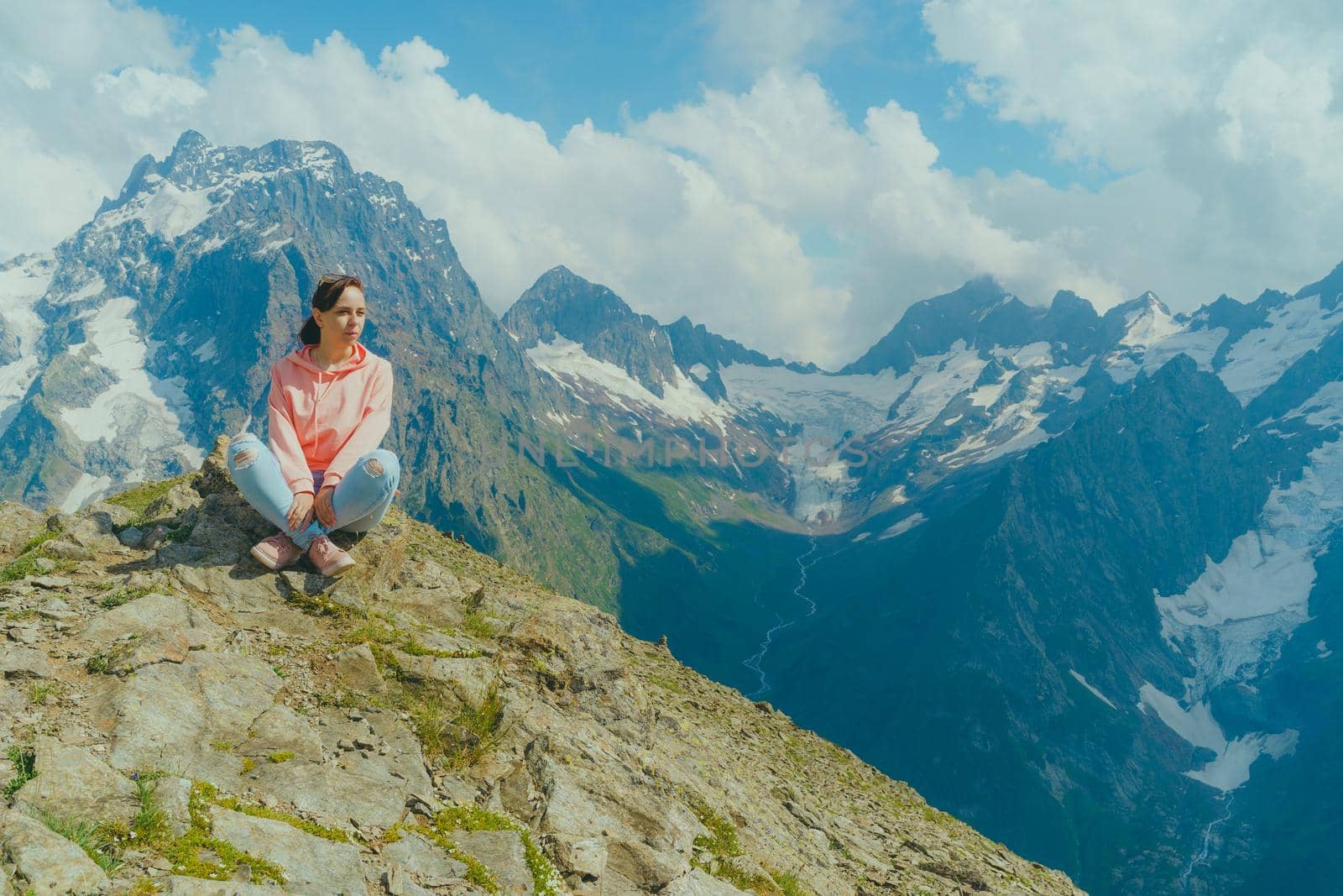 Young woman sitting on rock and looking at mountain landscape. Female traveler enjoying beautiful view in mountainous area. by epidemiks