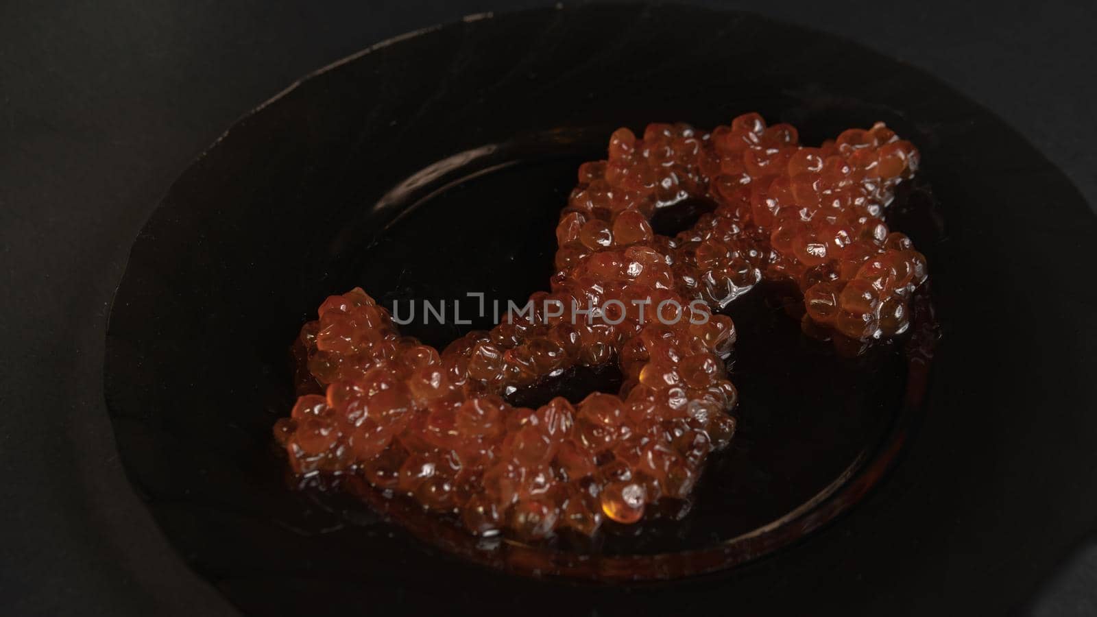 The dollar symbol at an angle is removed from a real bright red caviar on a black plate on a gray background view from above. Food in the world's elite restaurants is a symbol of money