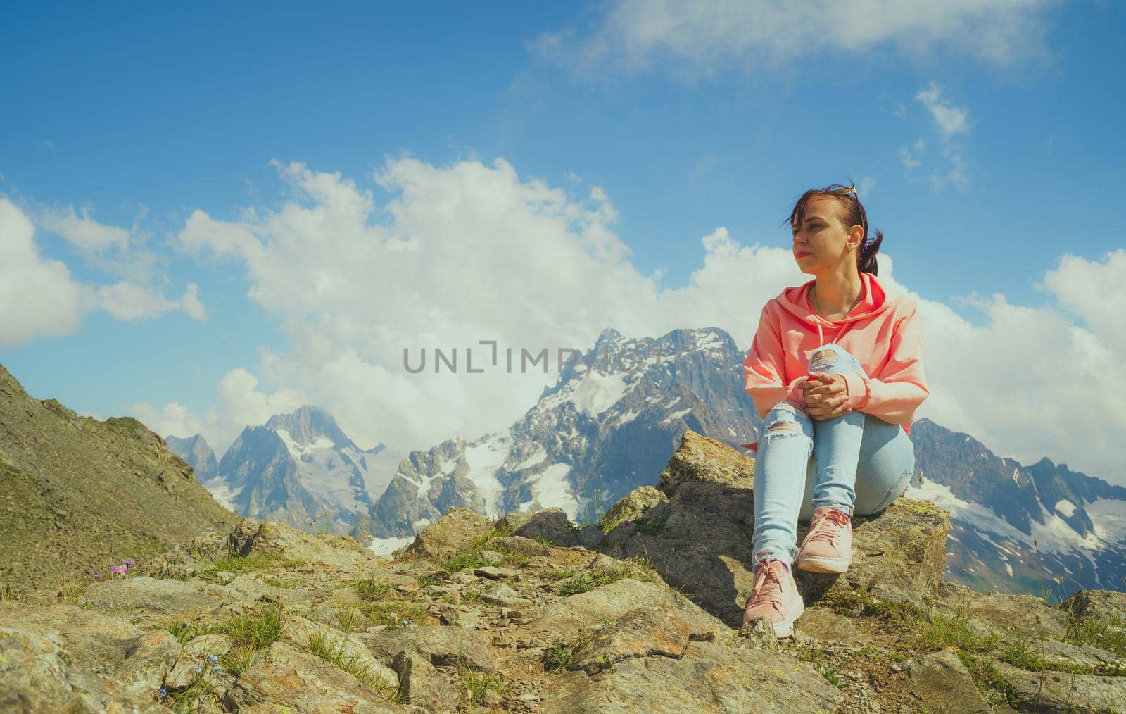 Young woman sitting on rock and looking at mountain landscape. Female traveler enjoying beautiful view in mountainous area. by epidemiks