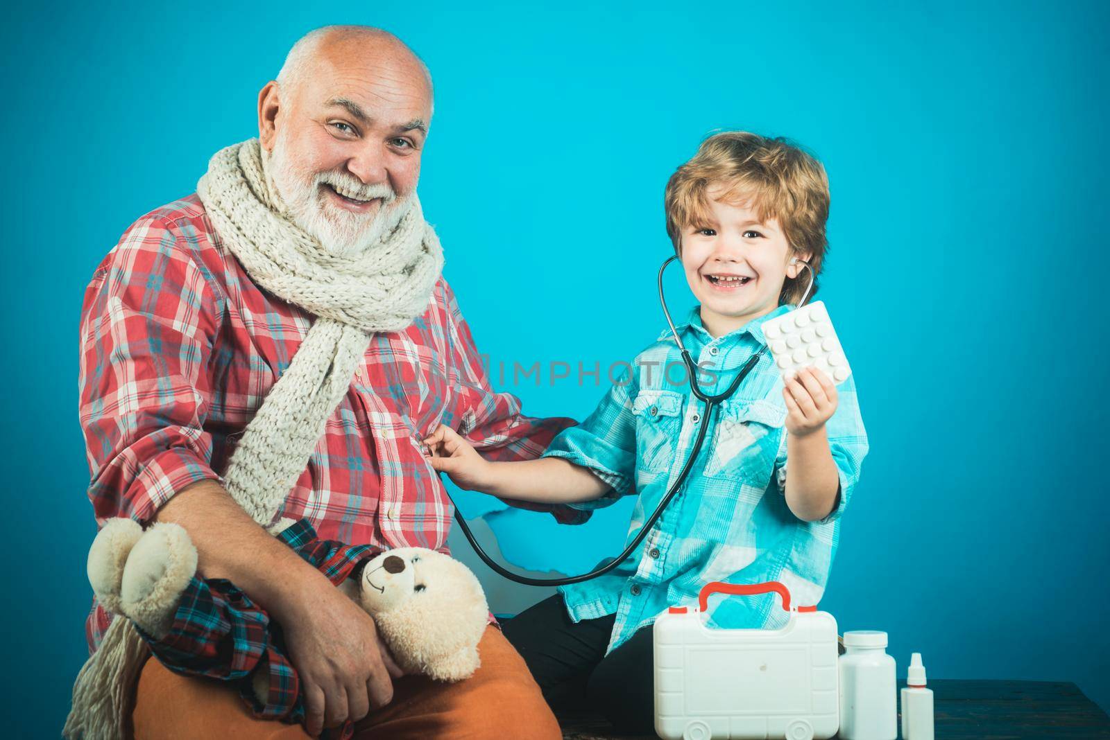 Little doctor grinning while showing tablet to old grandfather. Old man taking a pill. Little doctor. Grandfather and kid playing clinic