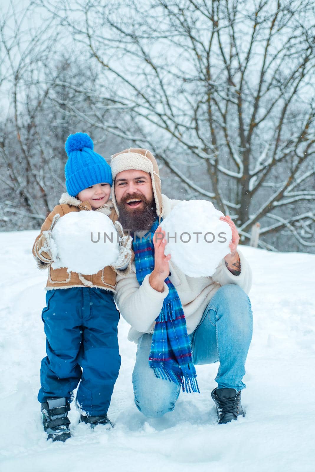 Best winter game for happy family. Happy father and son making snowman in the snow. Handmade funny snow man. Happy family plaing with a snowman on a snowy winter walk. by Tverdokhlib