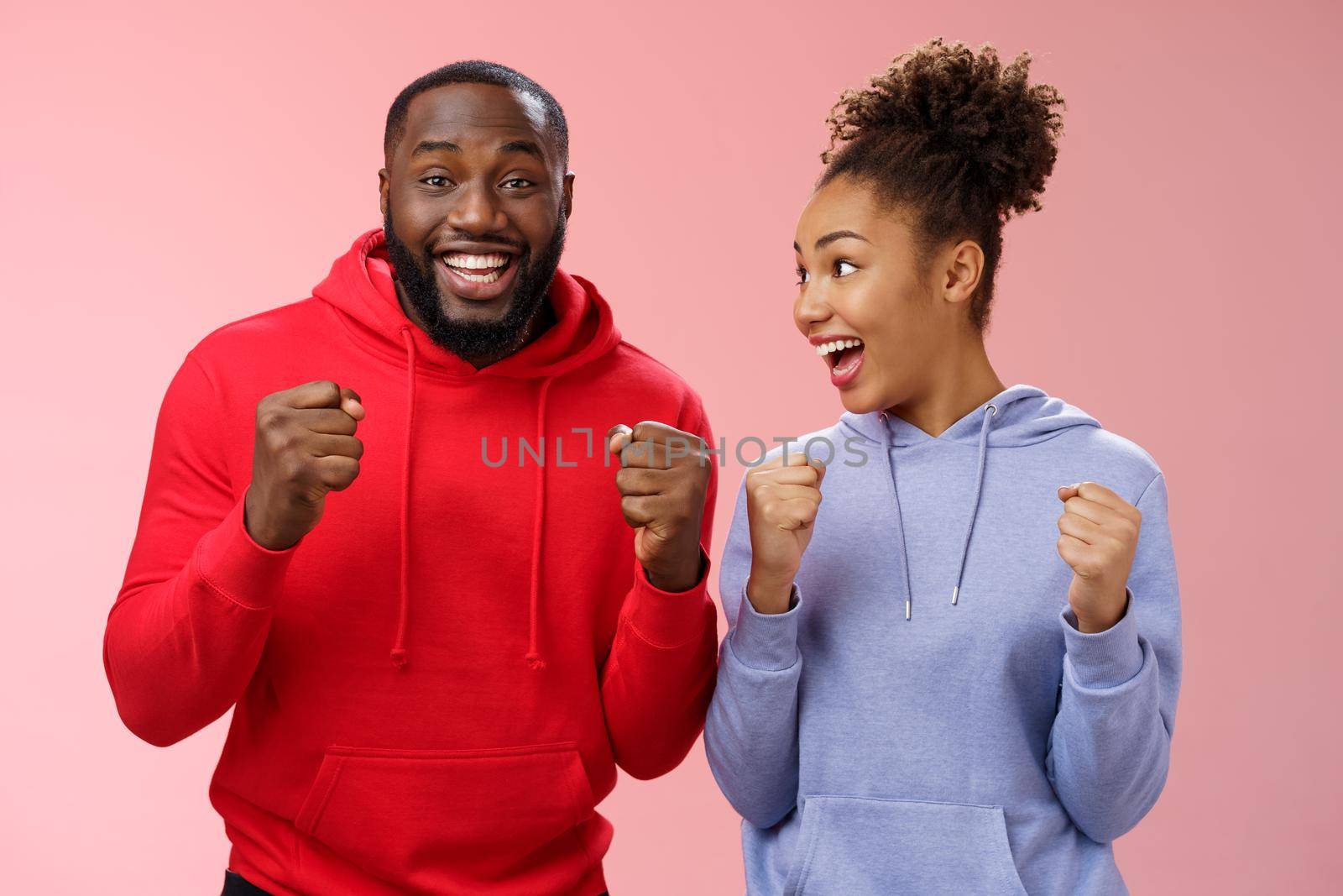 Joyful delighted celebrating african-american woman man standing together happy triumphing clenching fists cheering for favorite team watching match supporting fans celebrating goal win bet.