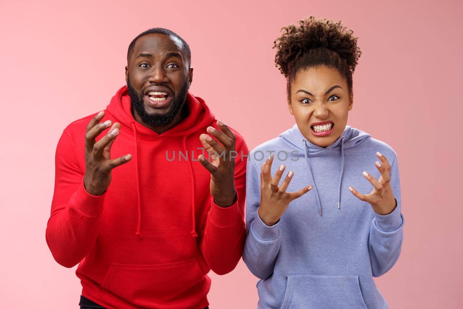 Two siblings upset failure losing bet watching football match cringing sorrow reckless, raising hands dismay sadness express regret anger being disappointed, standing pink background distressed.