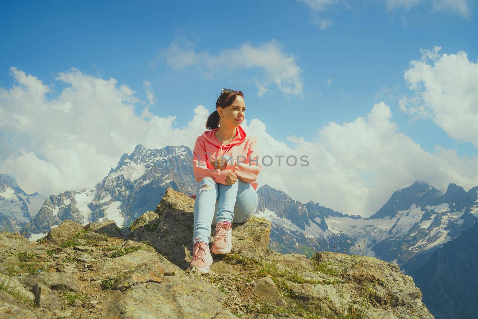 Young woman sitting on rock and looking at mountain landscape. Female traveler enjoying beautiful view in mountainous area. by epidemiks