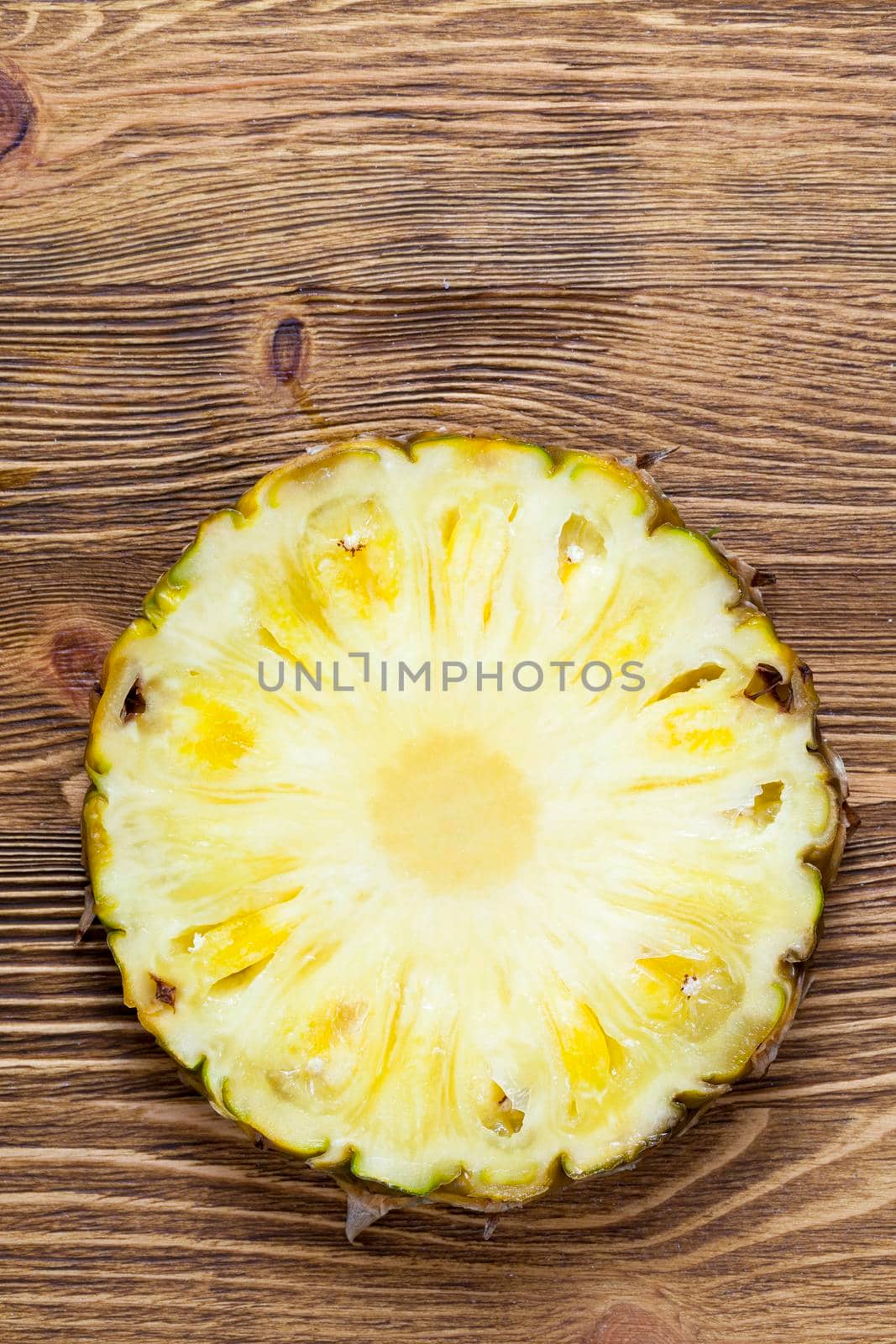 cut across a yellow fresh pineapple, which lies on a wooden board, closeup