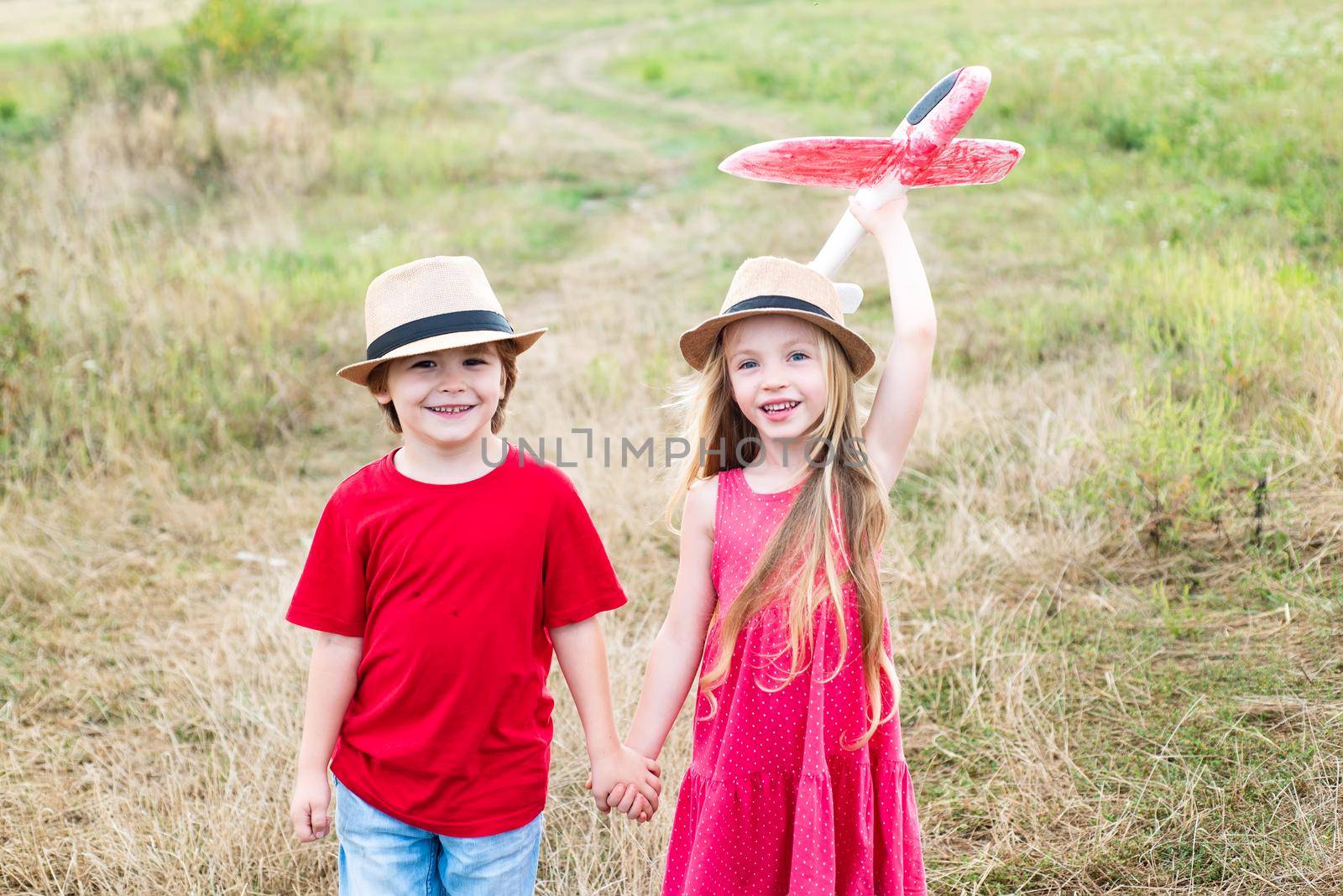 Summer holidays - love romance and people concept. First love. Two kids - boy and girl having fun with toy airplane in field. Happy children enjoying summer vacation