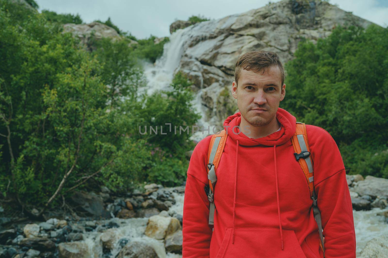 Portrait of young man looking away on background of waterfall. Adult male tourist enjoying beautiful view in mountainous area. by epidemiks