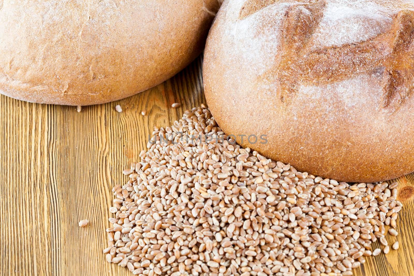 a loaf of whole grain bread and wheat grains stacked on a wooden table, closeup from the top