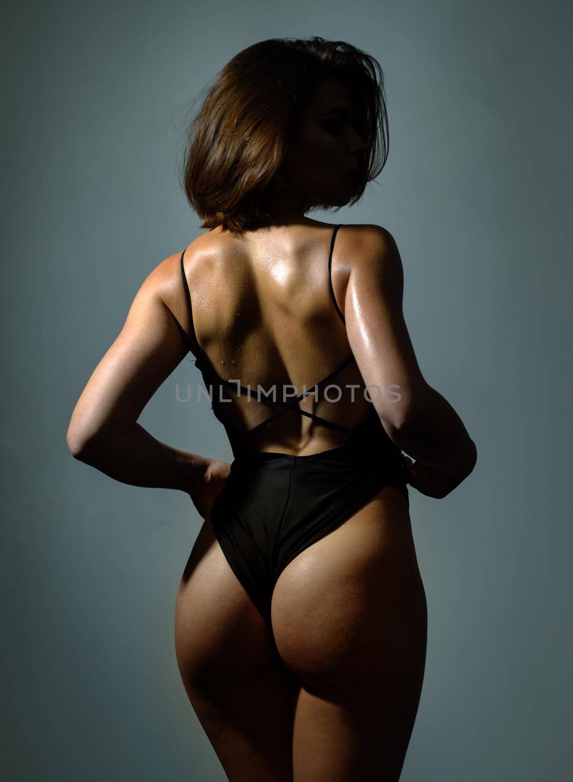 Sexy back beautiful ass slim woman with short dark hair isolated at grey background. Adorable charming woman with perfect body wearing sexy black lingerie. Hot butt concept