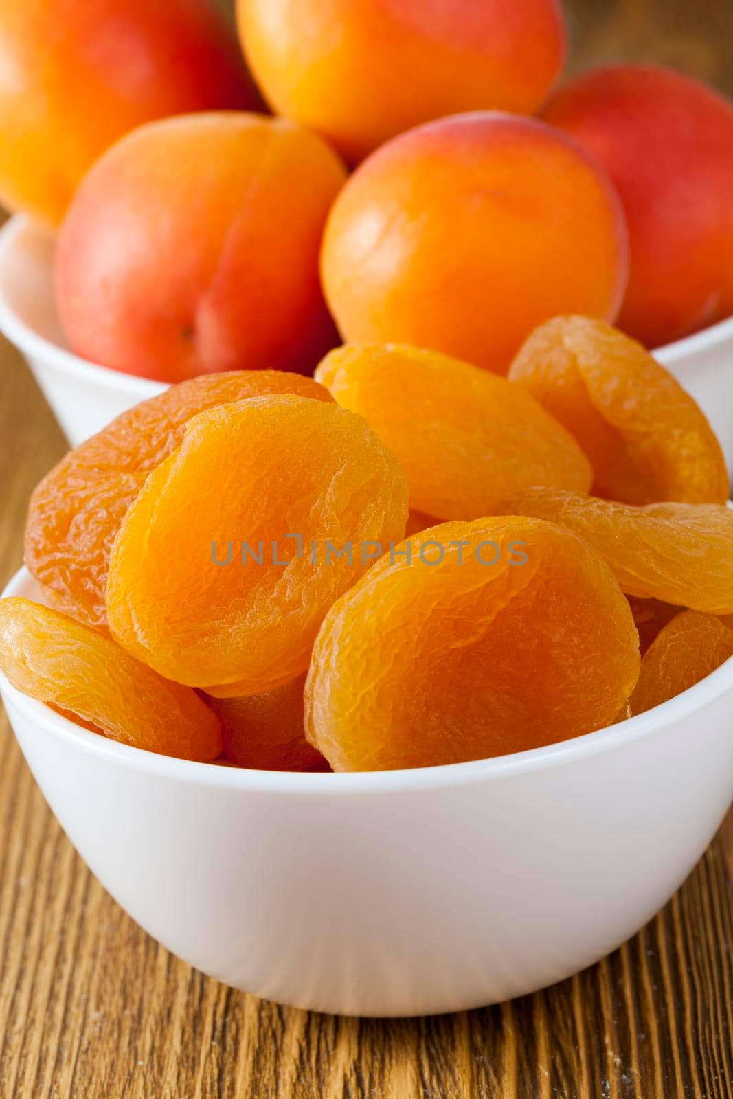 dry beautiful apricots in a bowl and ripe fresh apricots lying in another bowl in the background, closeup