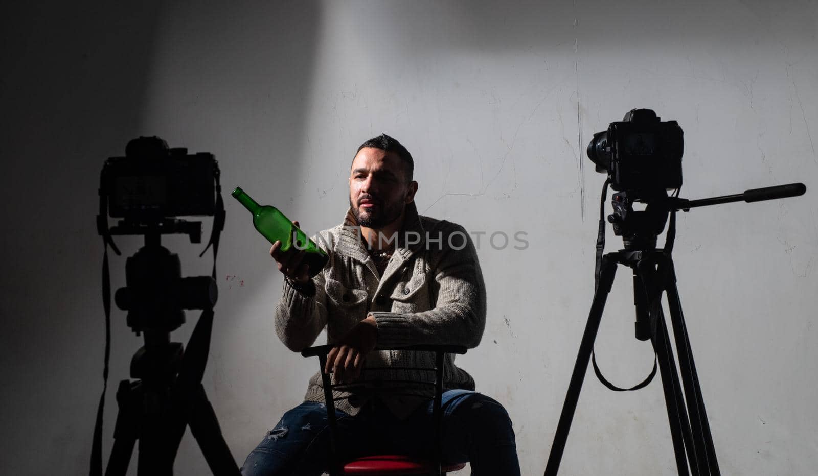 Man with bottle sitting. After a photo shoot with a bottle of alcohol. Professional camera. Handsome bearded man. Portrait of thinking stylish young man looking away