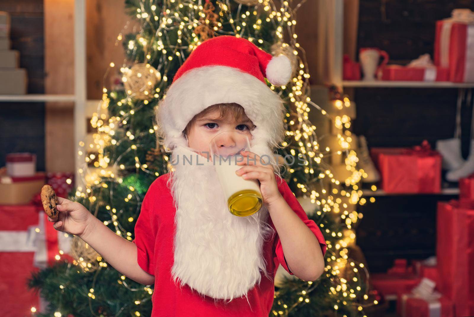 Santa kids picking cookie. Santa fun. Santa Claus takes a cookie on Christmas Eve as a thank you gift for leaving presents. Portrait of little Santa child holding chocolate cookie and glass of milk. by Tverdokhlib
