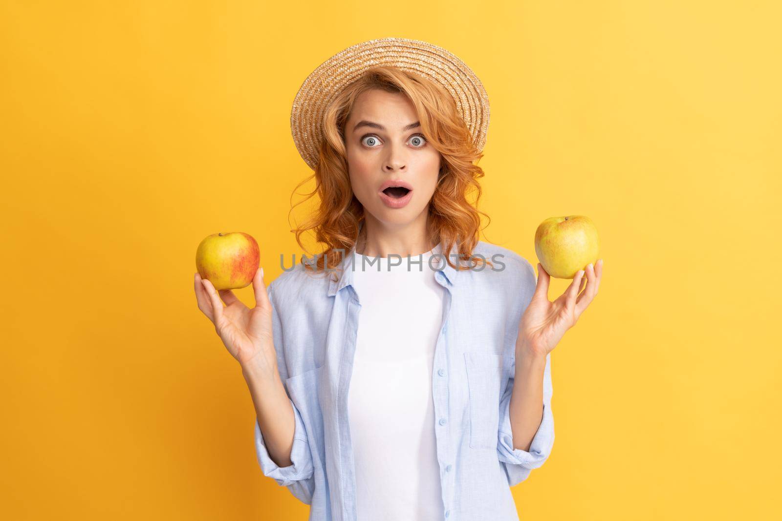 shocked young woman curly hair in summer straw hat with apple, detox.