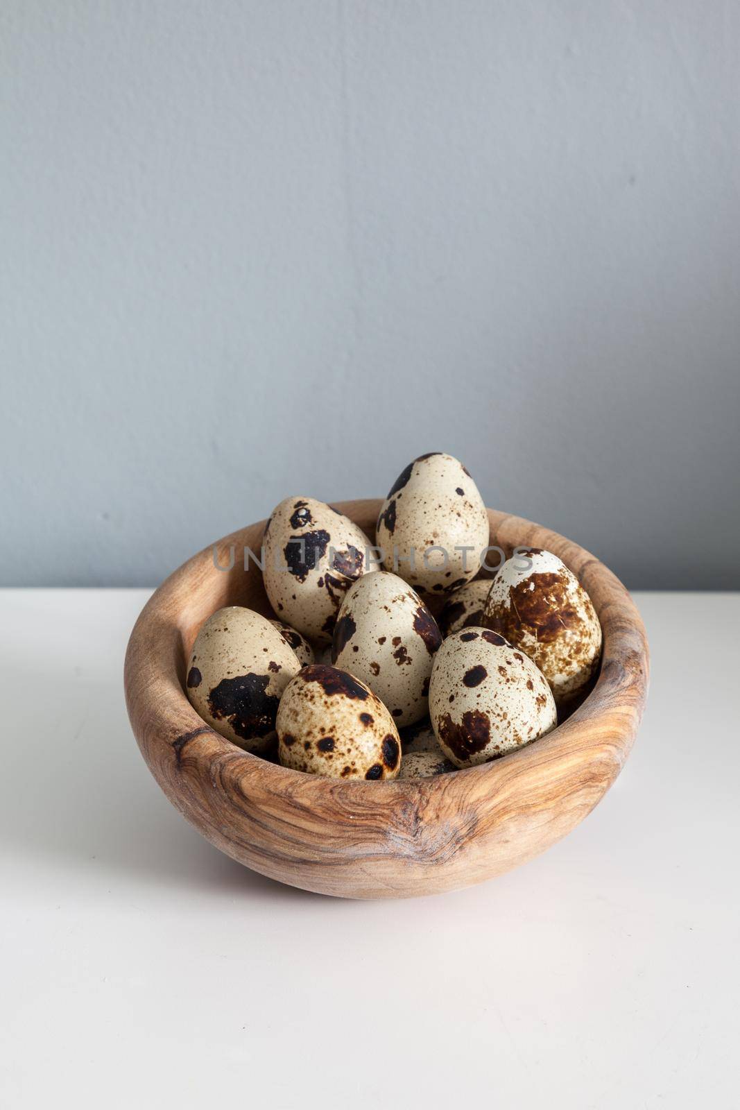 Speckled quail eggs in a wood bowl on a farm table by steffstarr