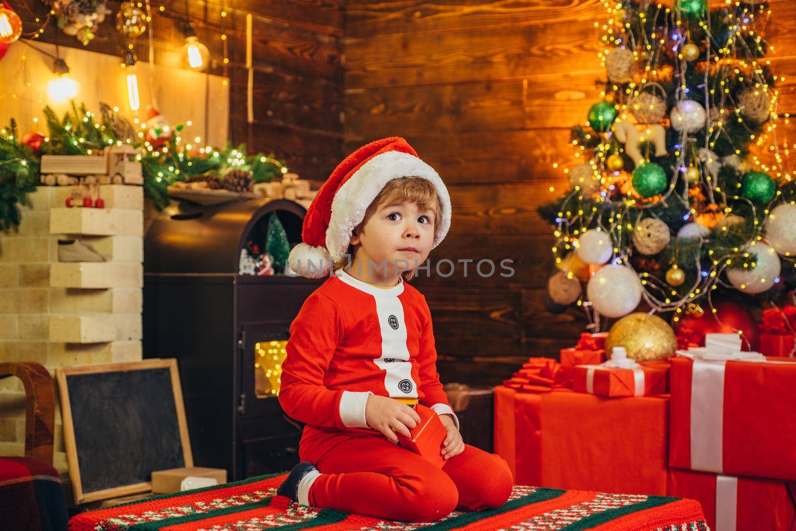 Cute little santa baby with New years gifts on Christmassy background. Celebrating Christmas together. Elf child. Gifts for winter holidays at fire place. It is a miracle