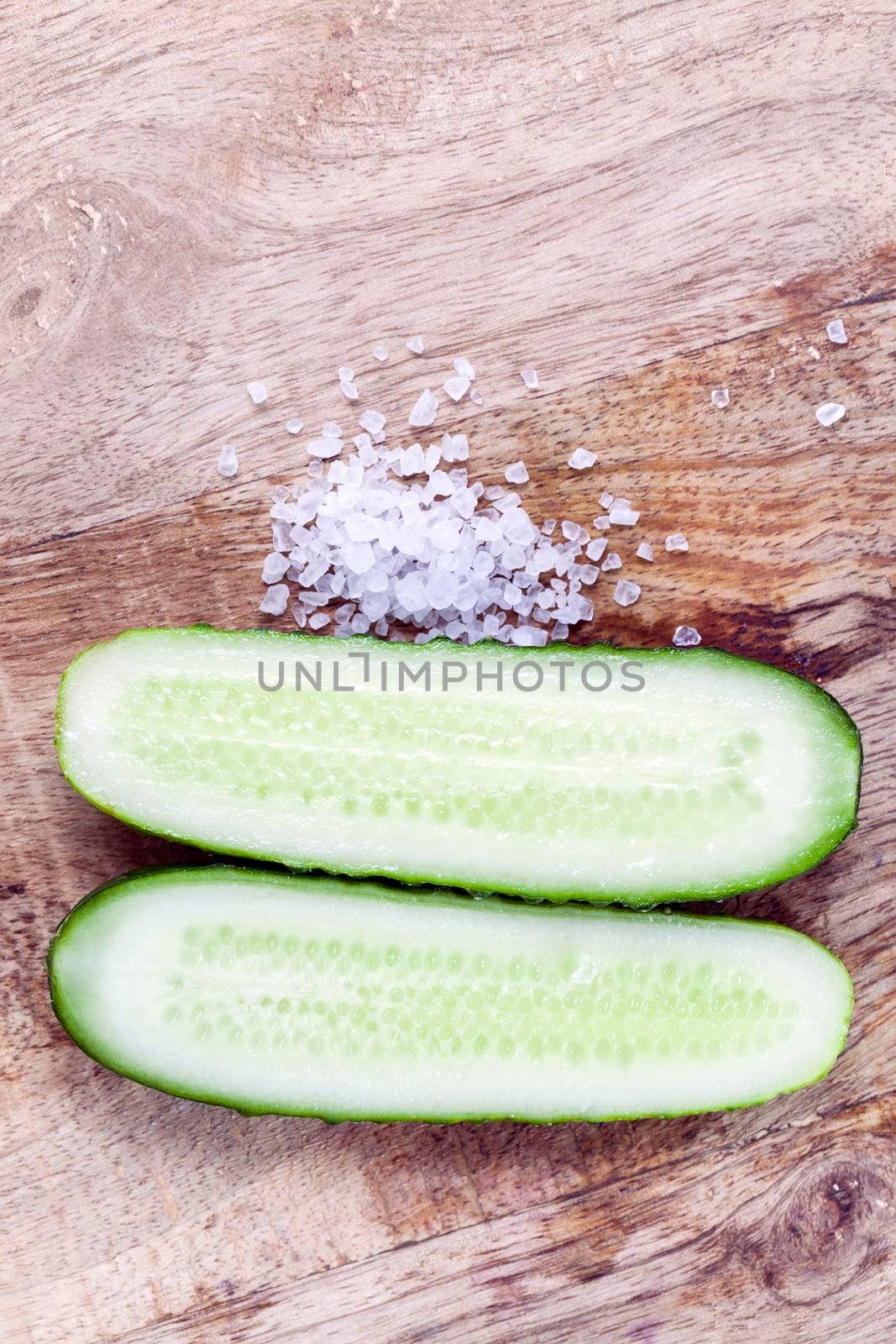 Sliced along a ripe green cucumber, salt and vegetables on a cutting board, closeup