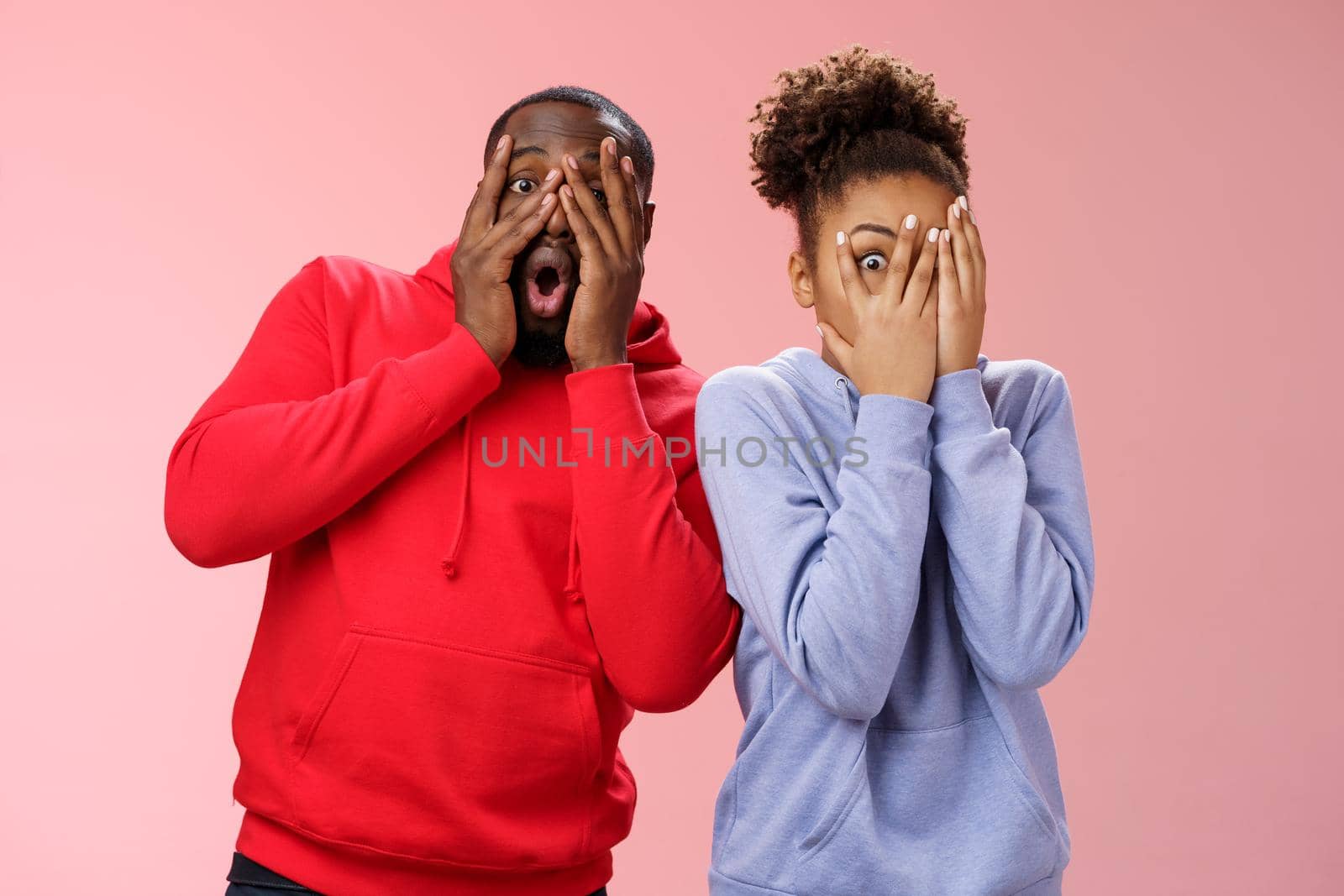 Funny cute carefree loving african american boyfriend girlfriend fool around hide faces palms peeking through fingers mimicking joking around make funny mimics, standing pink background surprised by Benzoix