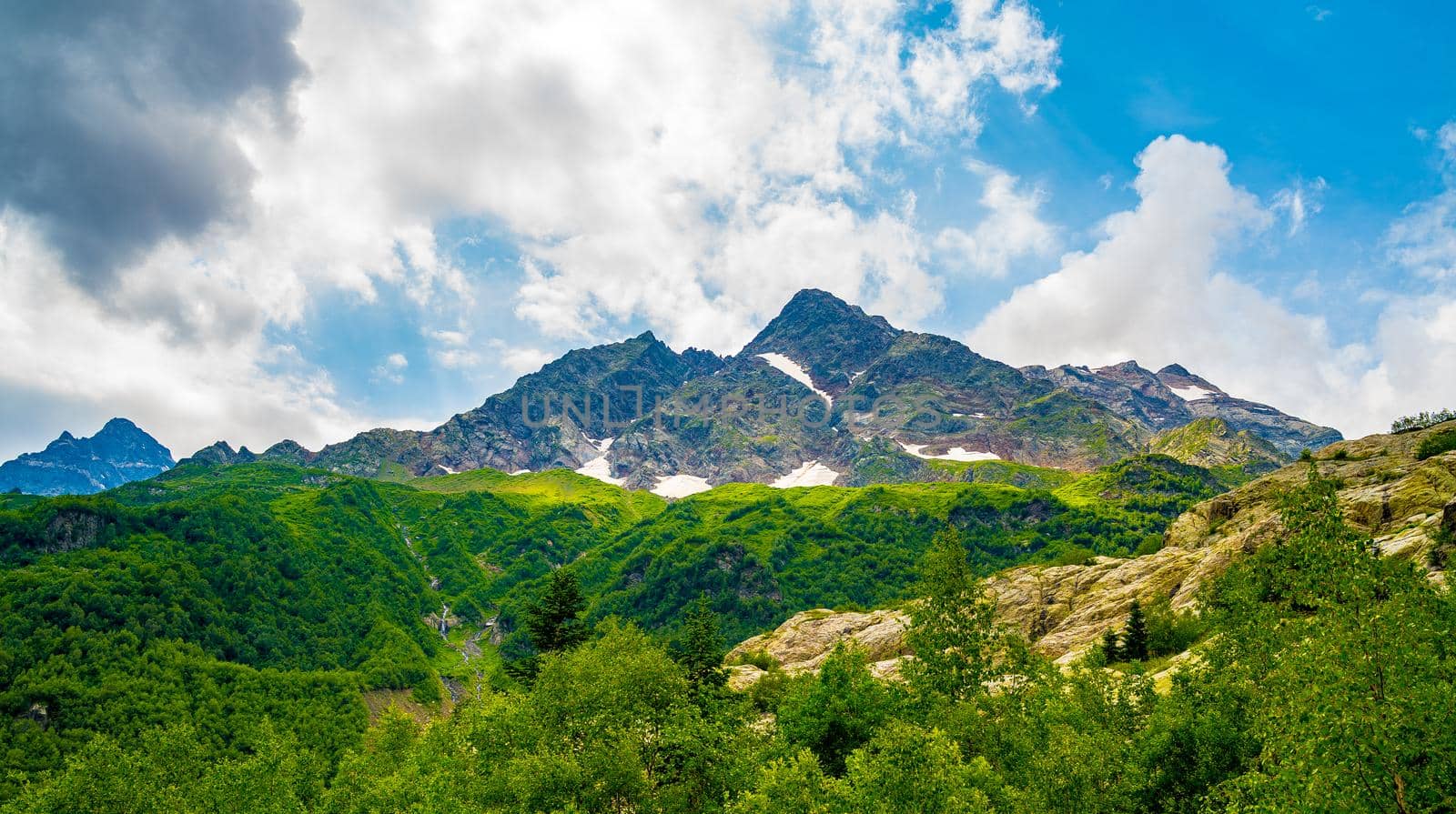 Mighty mountains with snow and green array in cloudy weather.