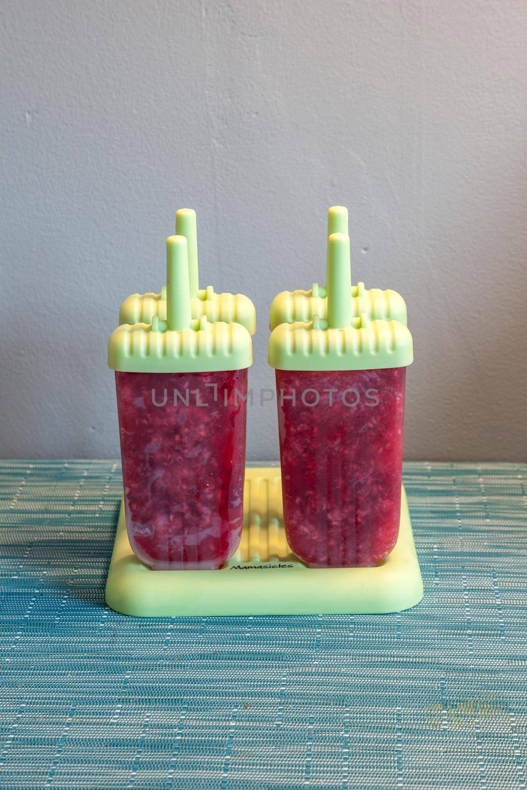 Homemade raspberry popsicles in a green mold during the summer heat.