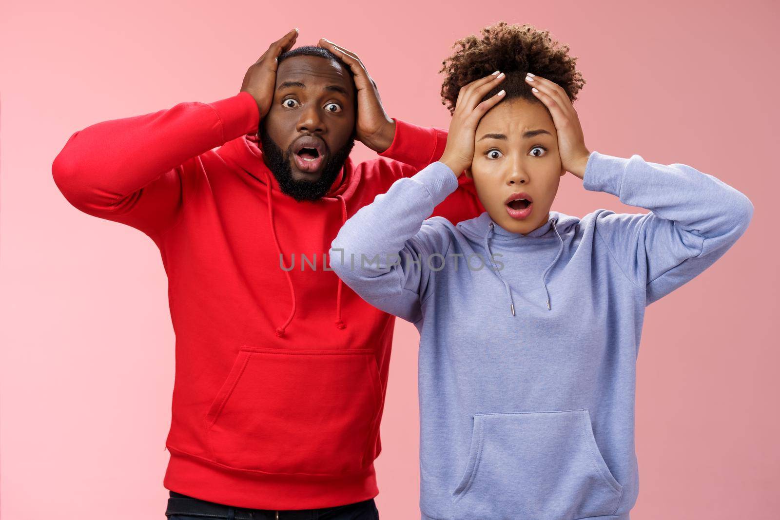 Shocked worried african american couple man woman holding hands head panicking widen eyes stunned receive bad concerning news feel troubled nervous, standing pink background anxious.