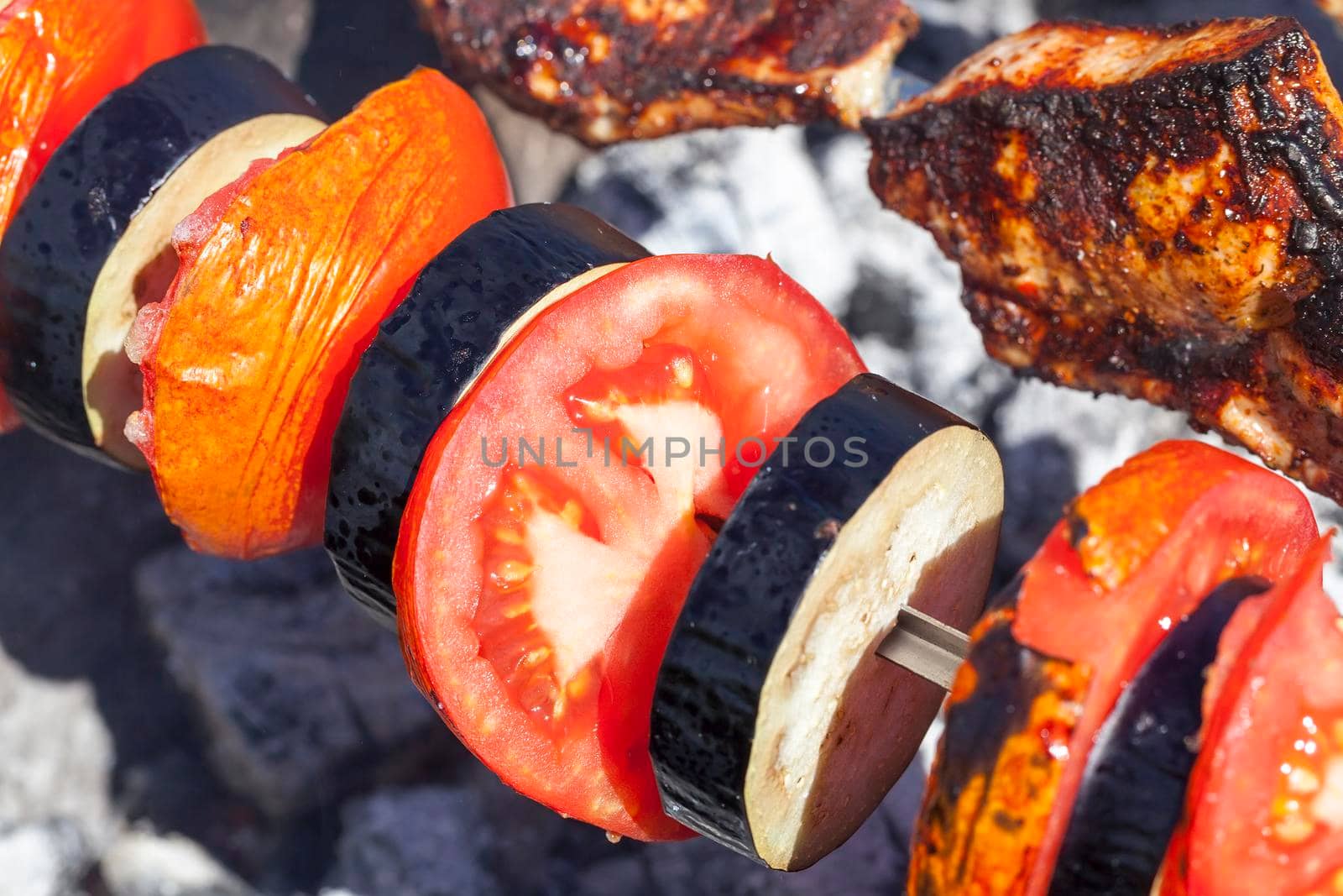 Vegetarian skewer with pieces of eggplant and tomato during cooking on fire, close-up