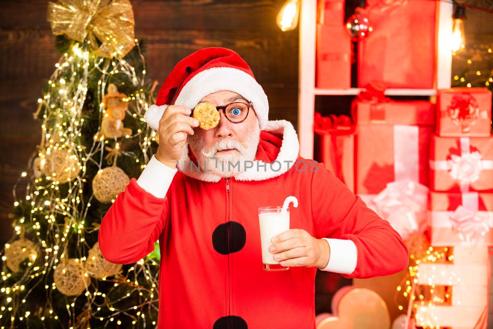 Santa Claus enjoying in served gingerbread cake and milk. Portrait of surprised and funny Santa. Christmas cookies and milk. Christmas for Santa Claus. Greeting Christmas card