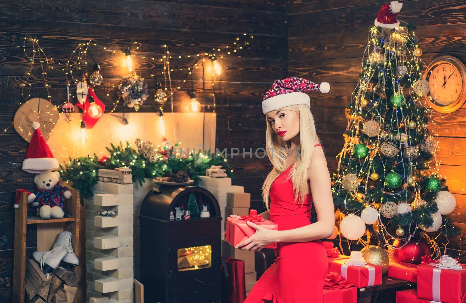 Happy woman with Christmas gift over Christmas interior background. Woman in red dress near the Christmas tree. Colorful makeup and retro hairstyle for Christmas or new year party