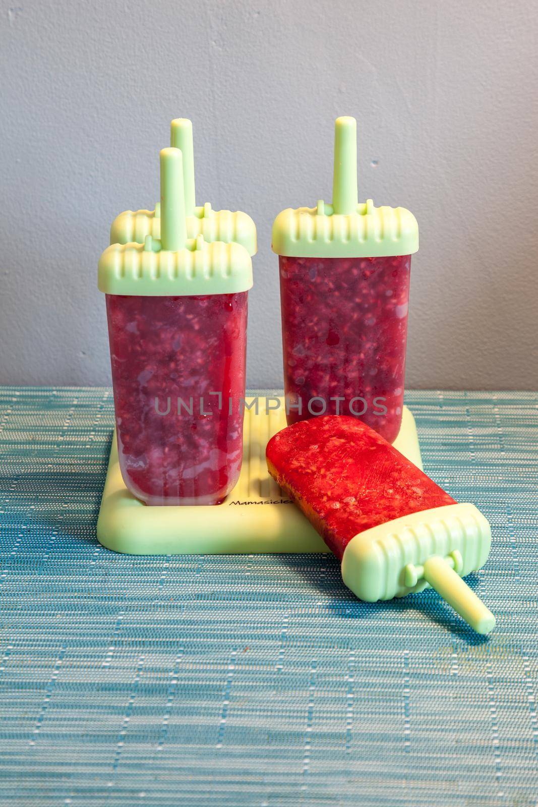 Homemade raspberry popsicles in a green mold during the summer heat.