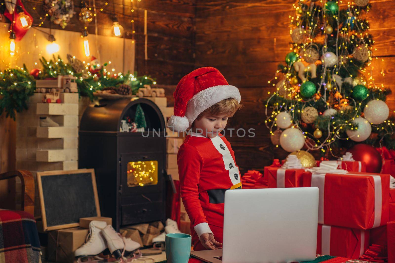 Smart toddler surfing internet. Santa little helper. Little boy santa hat and costume. Boy child with laptop near christmas tree. Buy christmas gifts online. Christmas shopping concept. Gifts service.