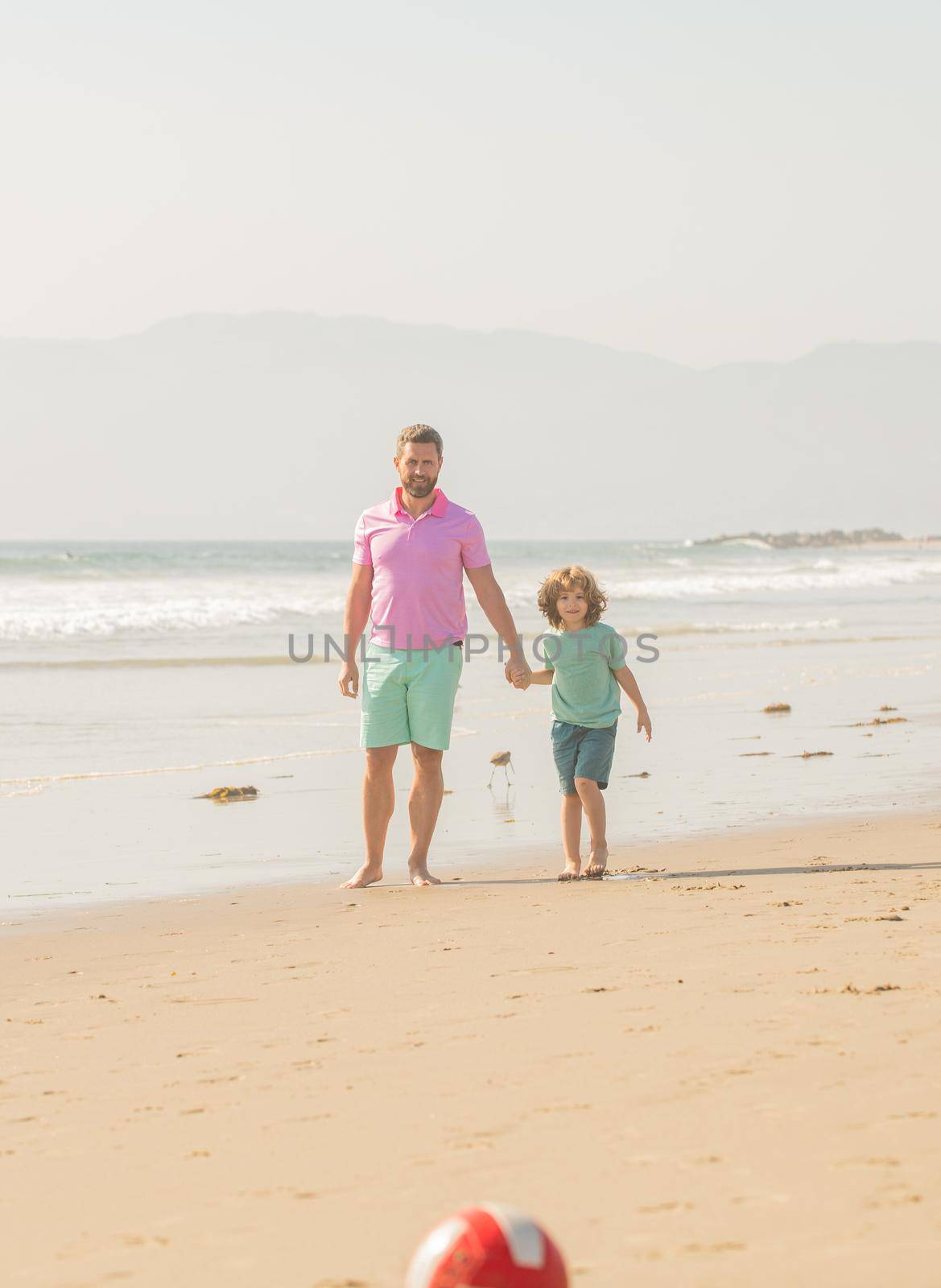 weekend family day. dad and child having fun outdoors. childhood and parenting. family holidays. sport activity. father and son play football on beach. daddy with kid boy on summer day.