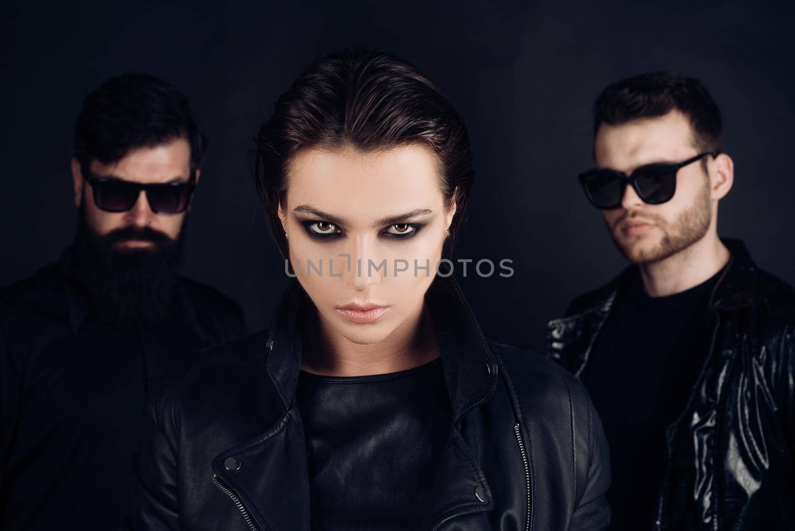 Closeup of young woman and handsome bearded men. Two stylish men in suits and girl in an black clothes. Young woman standing between two men. Company of confident people friends. Isolated on black