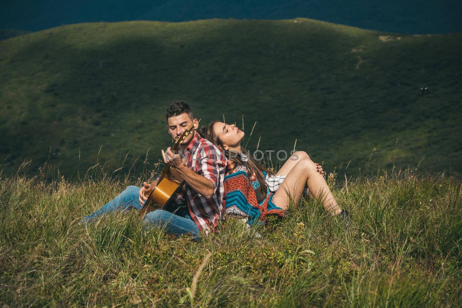 Happy travelers getting rest and playing guitar. Active lifestyle and amazing mountains concept. Smiling woman flirt with handsome man at the mountainside having rest at the nature