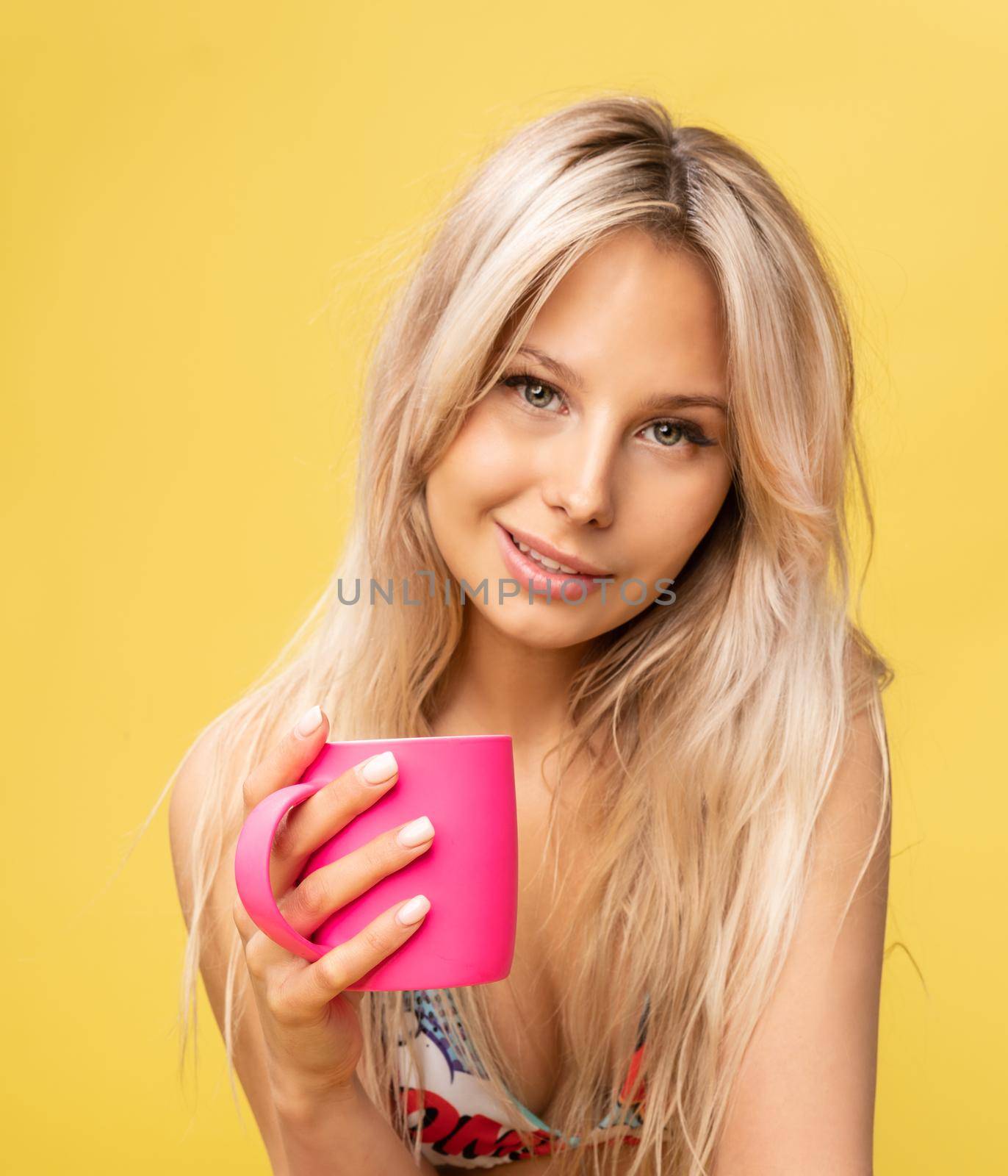 A girl sitting on the floor with her feet cross-legged keeps her head on a beautiful yellow background with a cup in hand yellow or pink and red fashion cheerful girl, pretty beautiful person, long sunglasses. Face busty, sun soppy