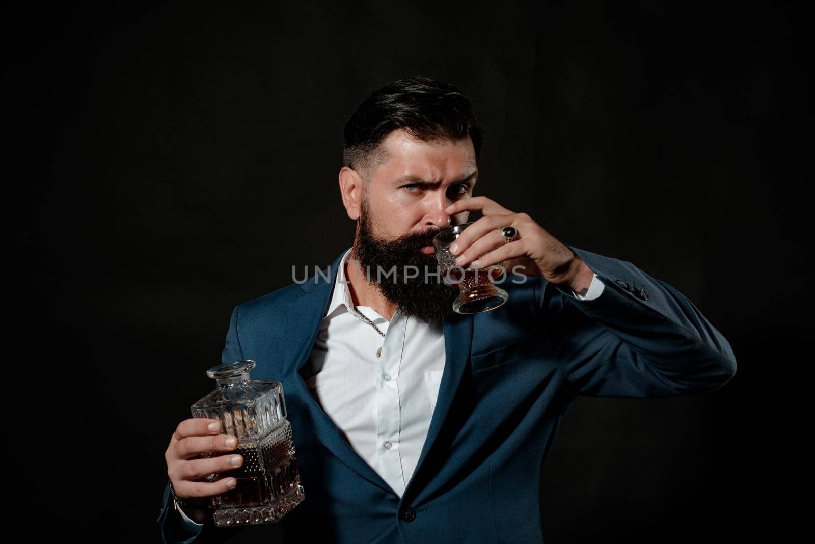 Man or businessman drinks whiskey on black background. Cheerful bearded man is drinking expensive whisky
