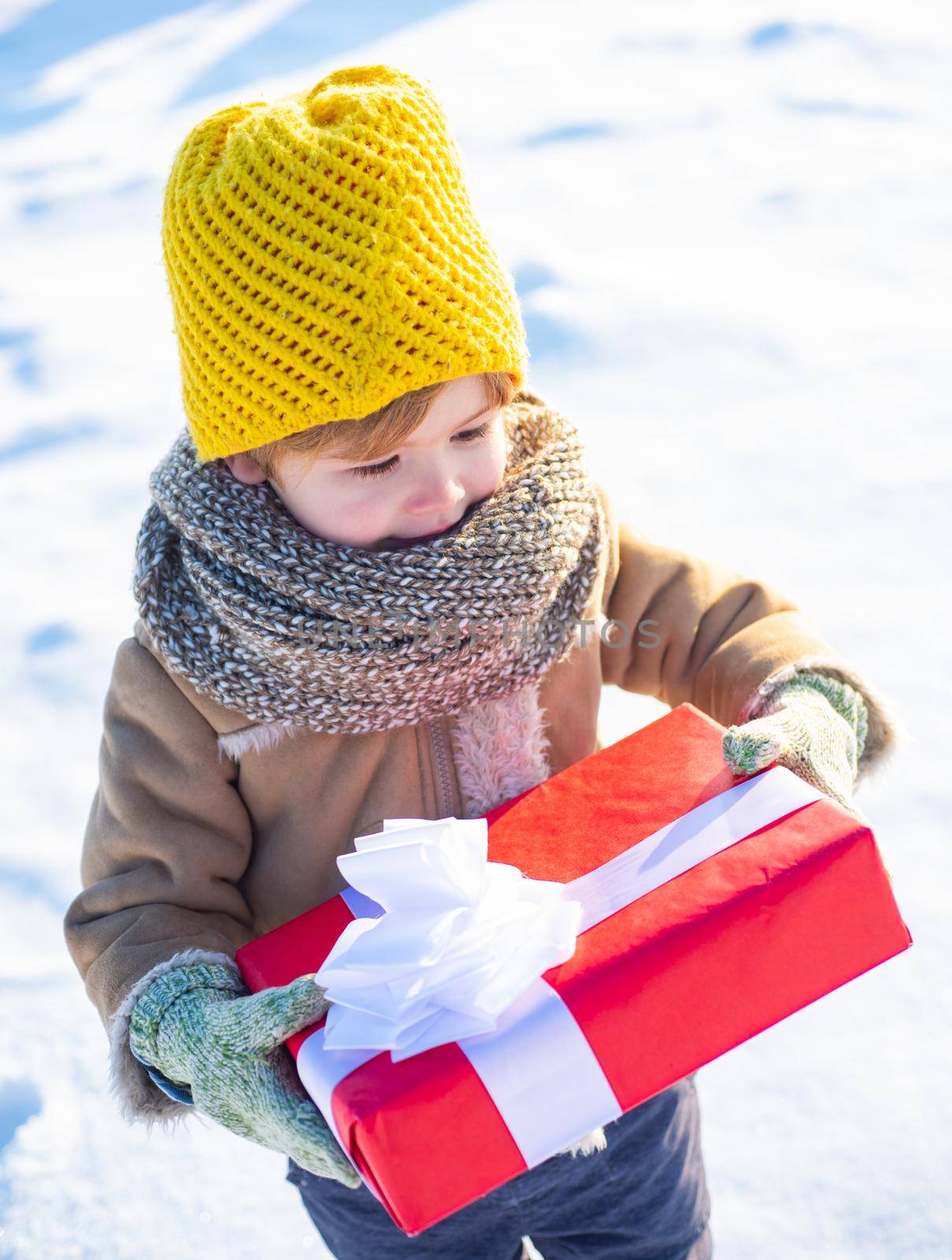 Little boy in warm winter clothes holding gift box and having fun. Bright clothes for children. Beautiful winter nature. Snow-covered forest path. Snowy cold weather concept