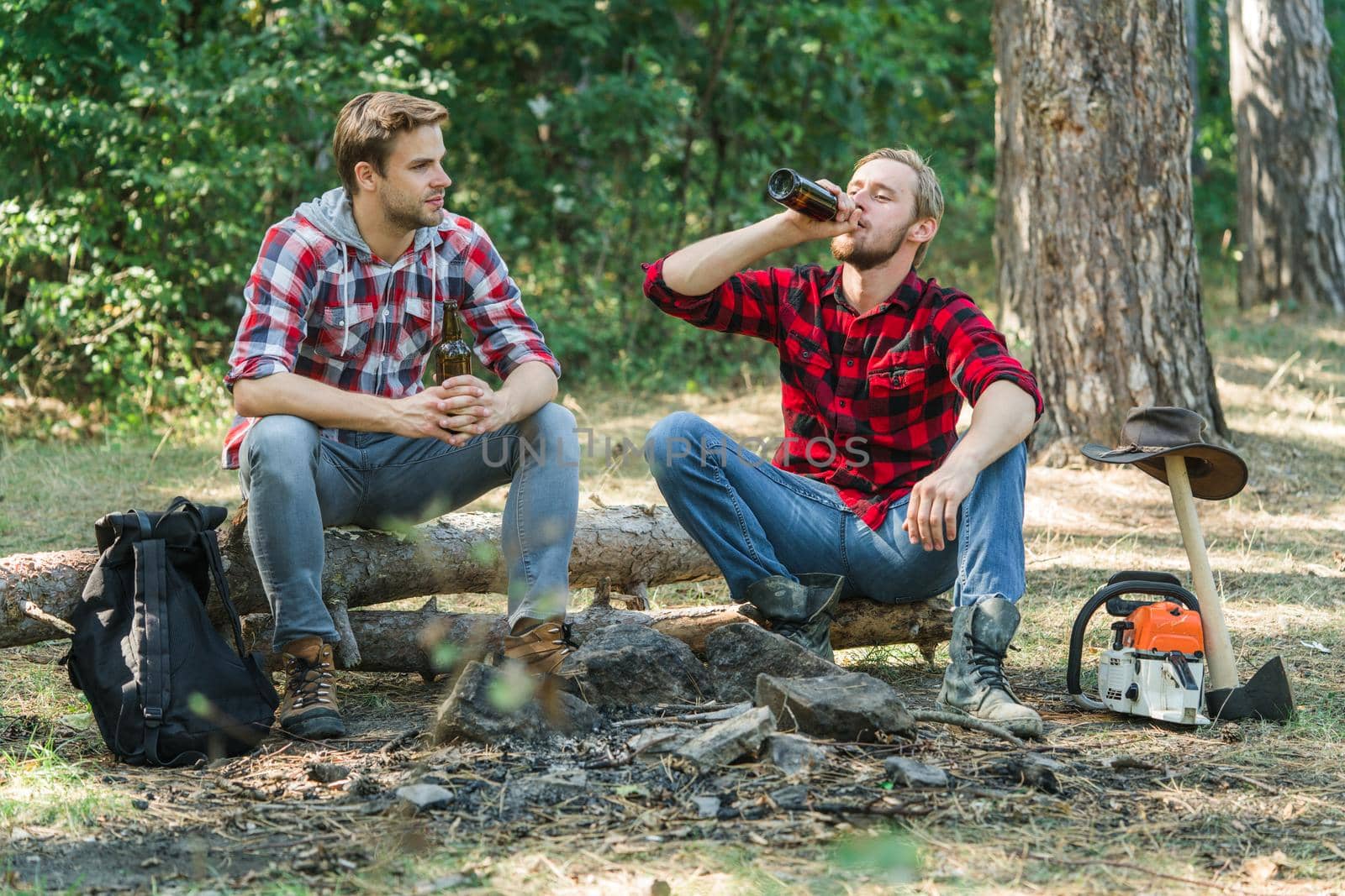 Young people having a camping. Picnic friends. Happy friends enjoying bonfire in nature. Company two male friends enjoy relaxing together in forest. Friends men hikers watching fire together on camp