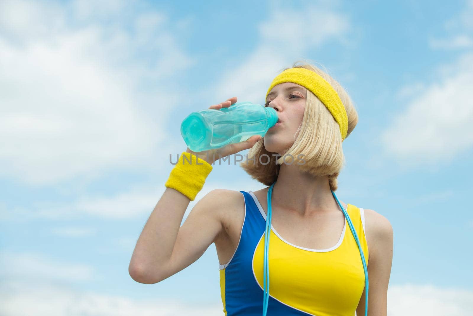 Blonde girl drinking water at sky cloudy background. Leisure time sport activities. Beautiful girl take care about her health drinking water and doing sport exercises outdoor