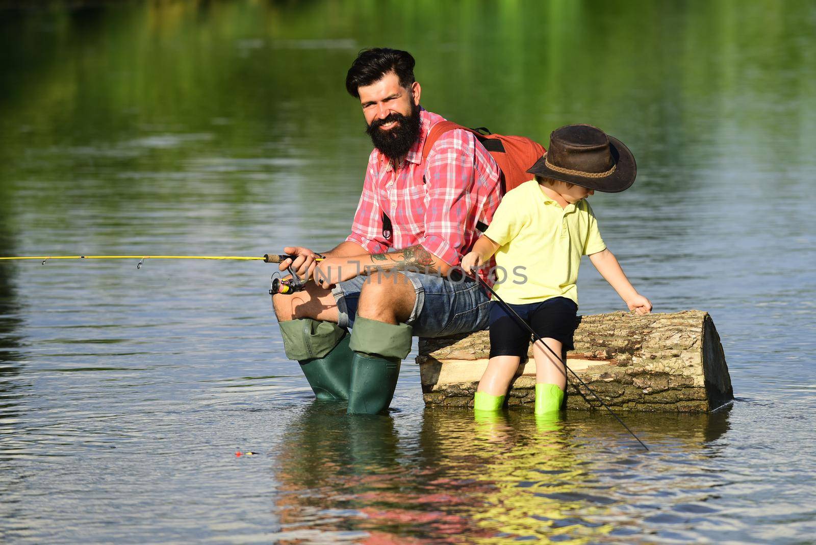 Father and boy son fishing together. His enjoys talking to father. Concept of a retirement age. Happy father and son fishing in river holding fishing rods